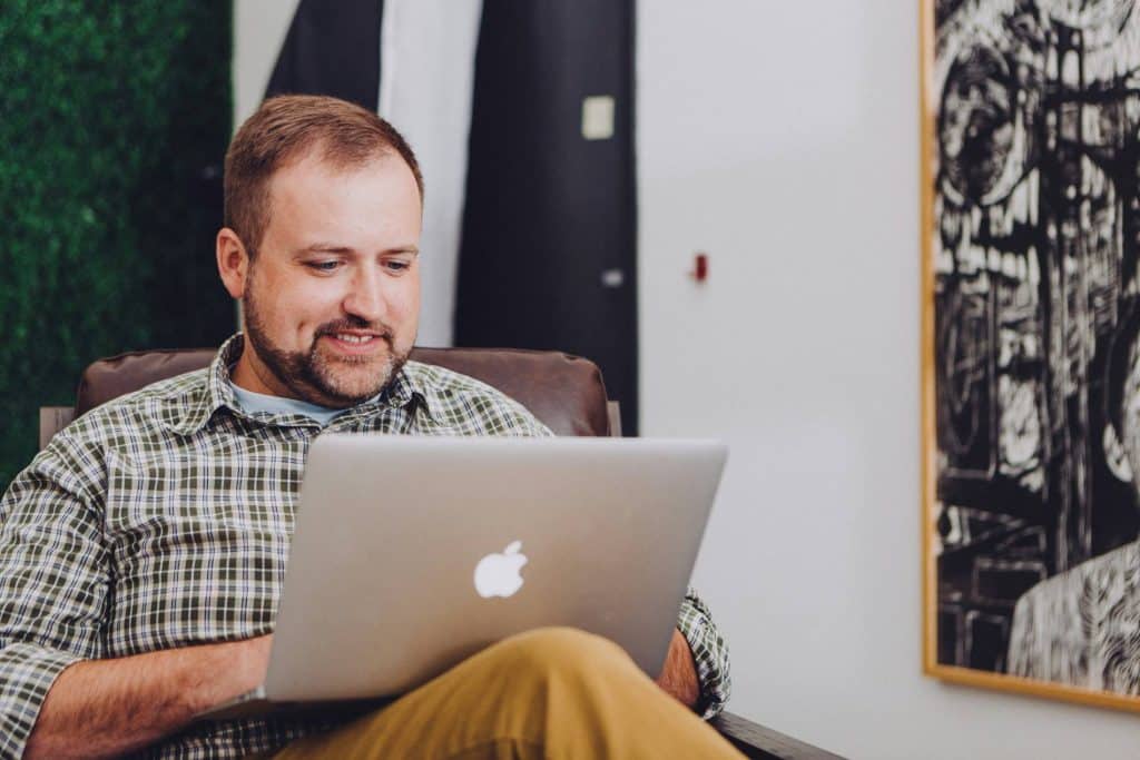 A man smiles while using his laptop computer on his lap.